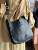 Model carrying the Herme$ Black Taurillon Clemence Leather Evelyne III PM with Palladium silver hardware