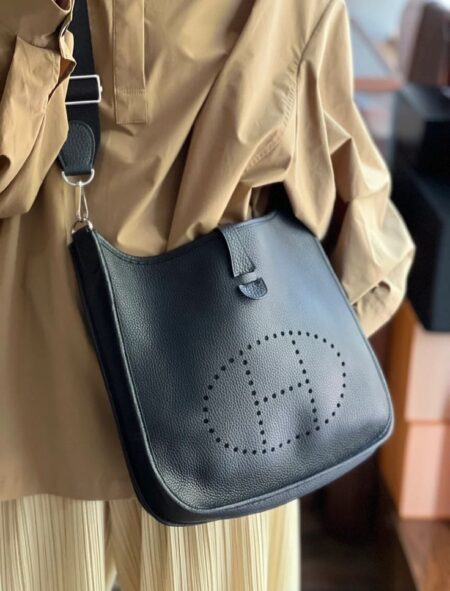 Model carrying the Herme$ Black Taurillon Clemence Leather Evelyne III PM with Palladium silver hardware
