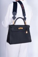 Model carrying the Herme$ Kelly Retourne 32 Black Togo Leather with gold hardware
