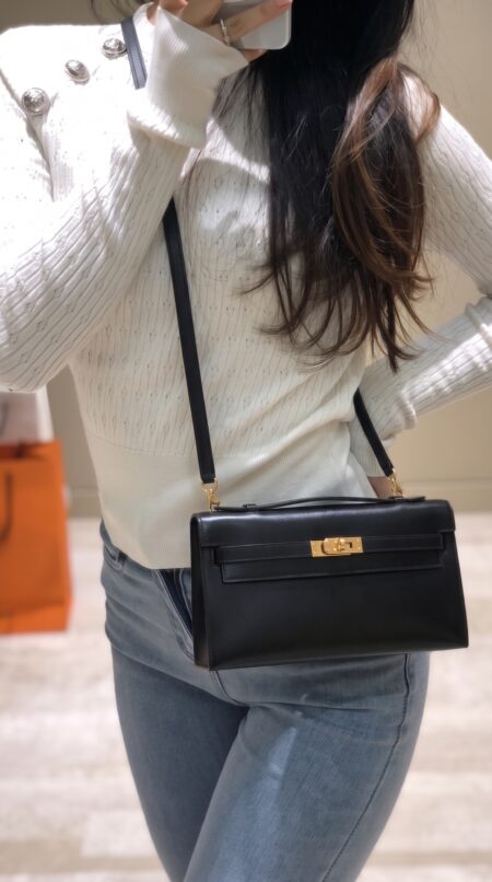 Model carrying the Herme$ Black Box Leather Kelly Wallet To Go with gold hardware