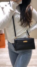 Model carrying the Herme$ Black Box Leather Kelly Wallet To Go with gold hardware