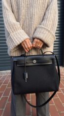 Model carrying the Herme$ Black Military Toile and Vache Hunter Leather Herbag Messenger 39 with Palladium hardware