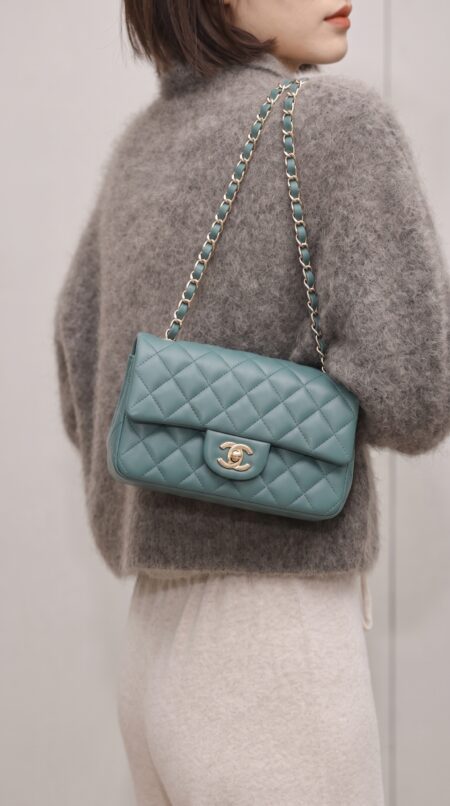 Model carrying the green lambskin ch@nel Mini Rectangular Flap with polished gold chain strap