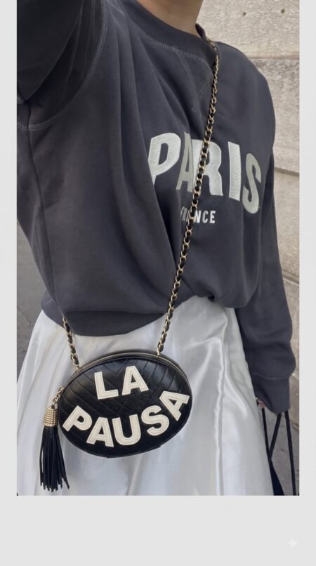 Model carrying the black lambskin Ch@nel La Pausa Tassel Clutch with light gold chain strap