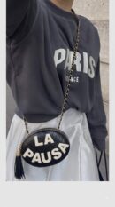 Model carrying the black lambskin Ch@nel La Pausa Tassel Clutch with light gold chain strap