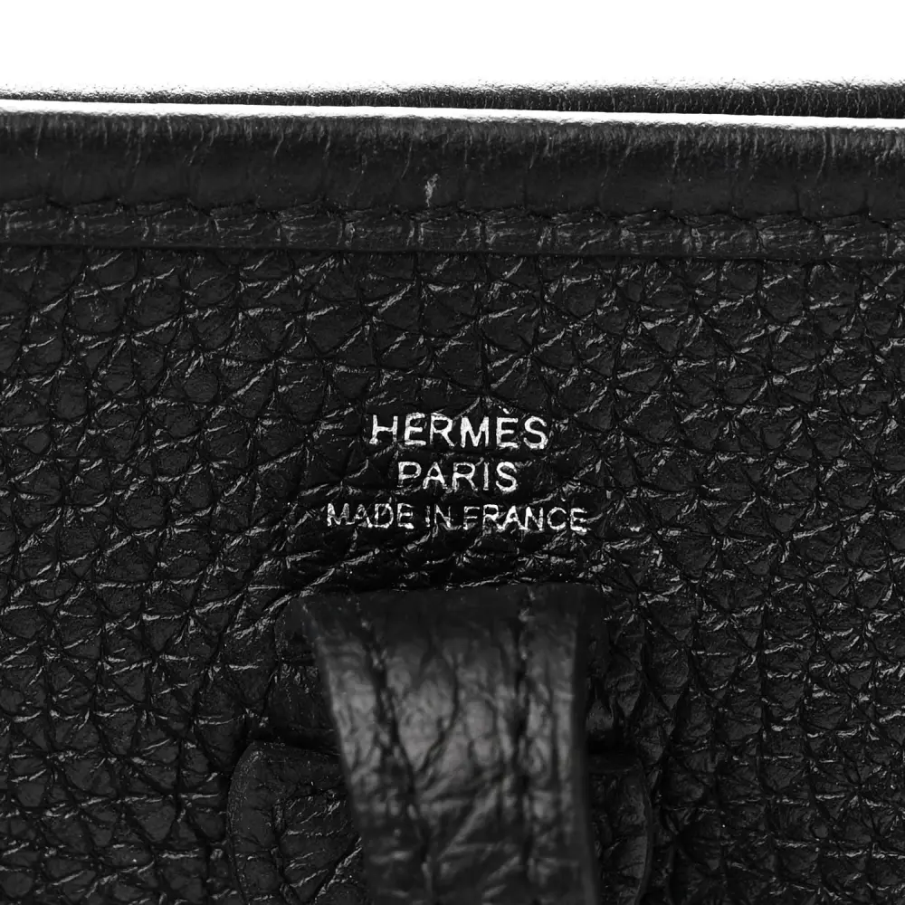 Close-up of the perforated H logo and Palladium hardware on the Herme$ Evelyne TPM