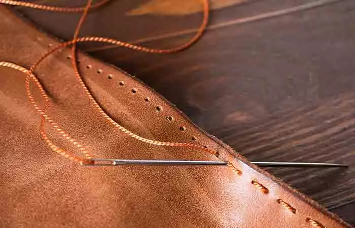 Hand-finished saddle stitching on super clone bags handle base showing 4 to 5 even stitches per centimetre versus machine stitching on AAA bag with loose uneven spacing