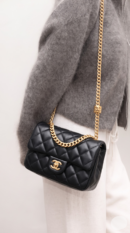 Model carrying the black Ch@nel Small Pillow Crush Flap with gold-tone chain shoulder strap