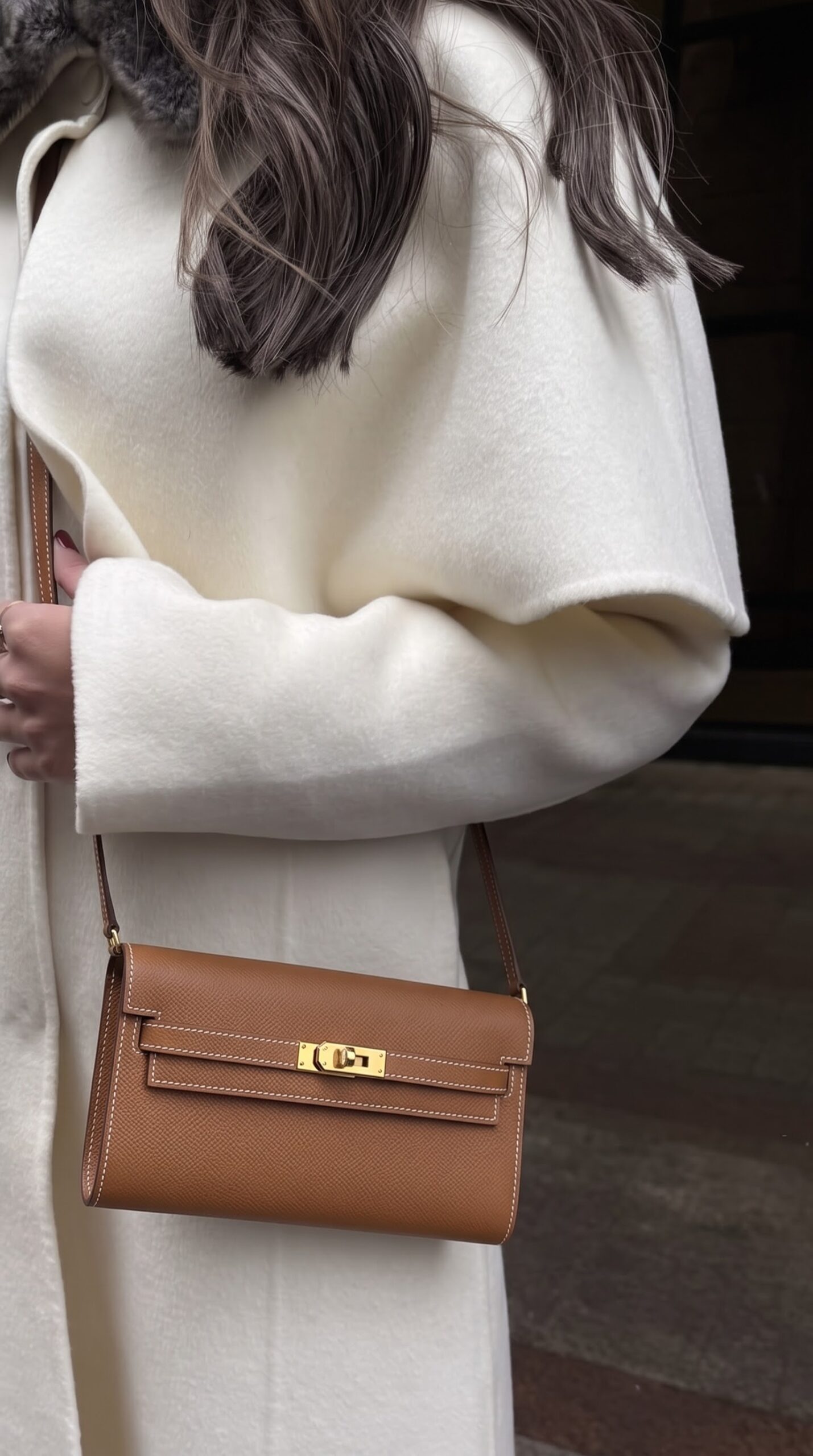 Model carrying the brown Epsom Herme$ Kelly Long Wallet To Go with its shoulder strap