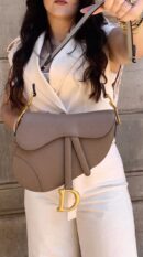 Model carrying the warm taupe D!0r Medium Saddle bag with adjustable shoulder strap
