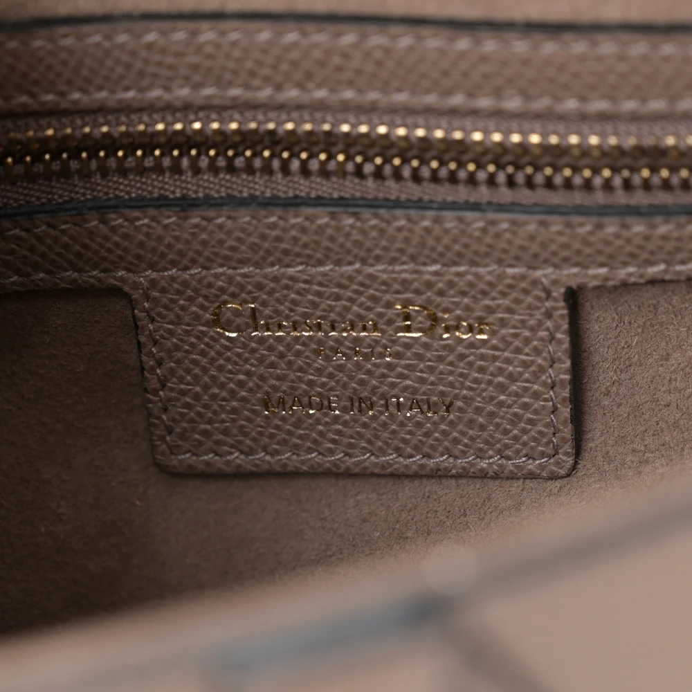 Close-up of aged gold-tone D logo and CD strap anchors on the taupe Saddle bag